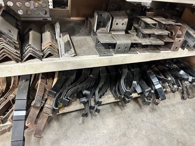 Shelves stocked with metal brackets and leaf springs in a workshop.