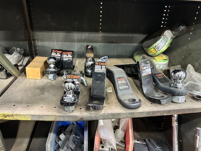 Assorted trailer hitch balls and components on a metal shelf in a shop setting.