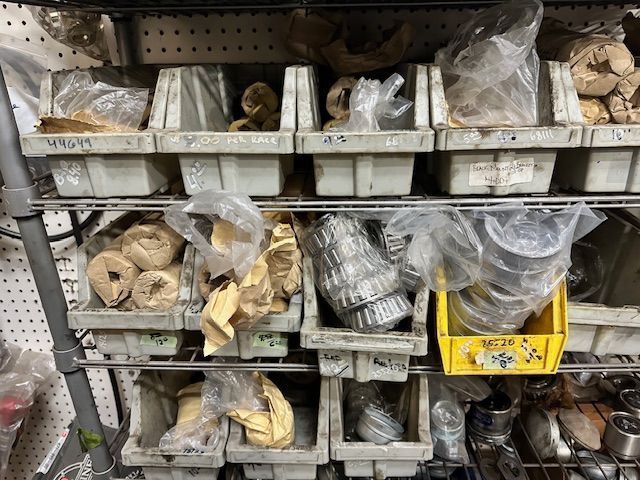 Shelves with bins of auto parts in a garage, including wrapped pieces and plastic bags.