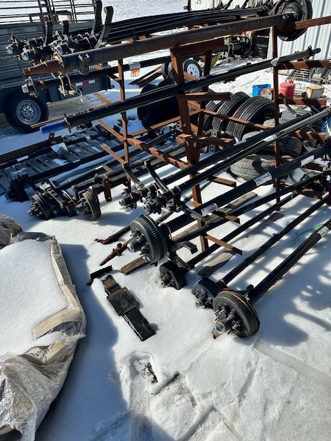 Trailer axles and parts scattered on snow, with a metal rack and trailer in the background.