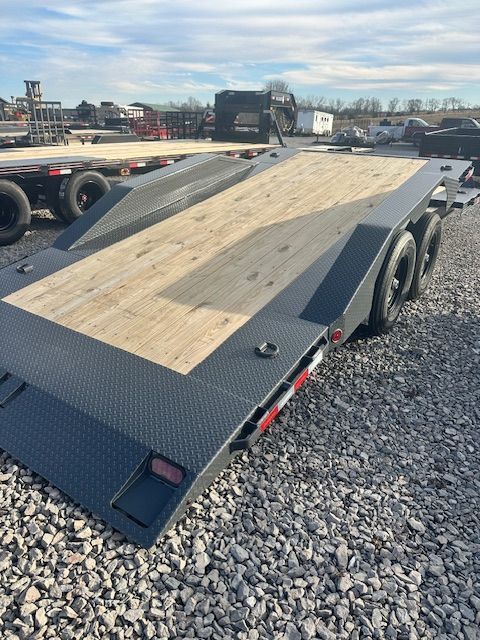 Black flatbed trailer with wooden deck on a gravel lot.