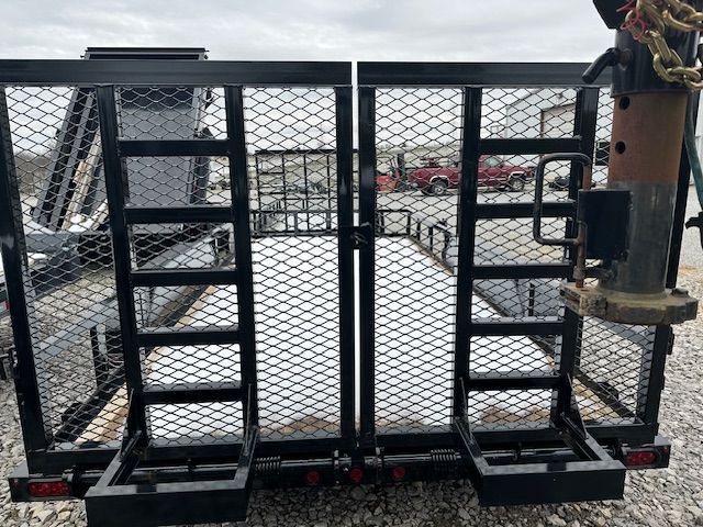 Black utility trailer with mesh gates, taillights, and trailer hitch against a cloudy sky.