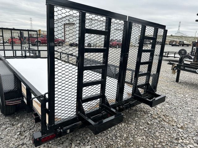 Black utility trailer with mesh sides and ramp supports, parked outside.