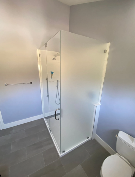 Modern glass shower enclosure with frosted glass, on a tile floor next to a toilet.