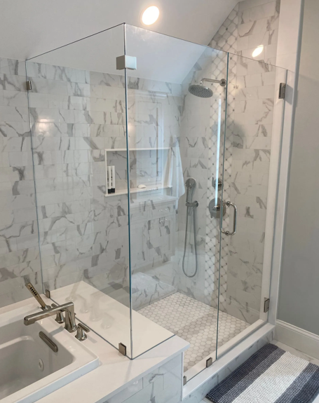 Modern glass shower with marble walls and a hexagon tile floor.