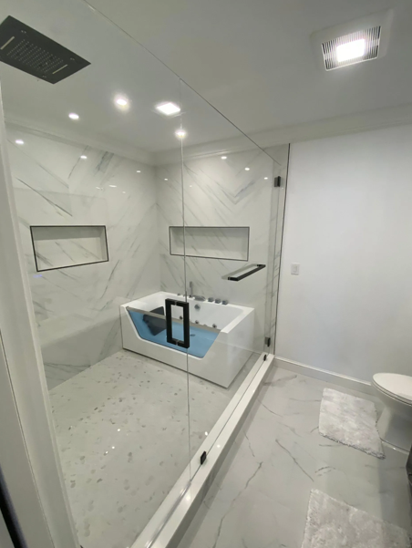 Modern bathroom with a glass shower, white tiles, a tub, and a toilet.