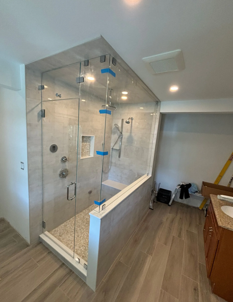 Modern bathroom with glass shower enclosure, gray tile walls, wooden floor, and a wooden vanity.