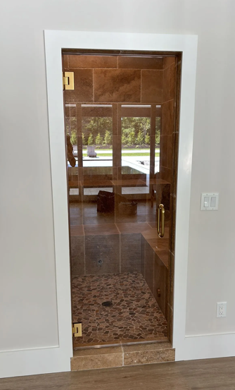 Shower with glass door, tiled walls and floor, framed in white, interior setting.