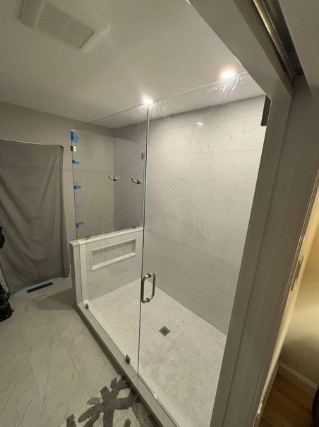 Modern shower with glass enclosure, white tile, recessed shelf, and sliding door.