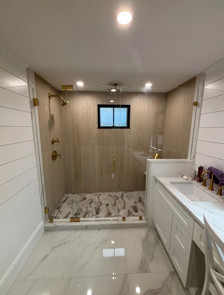 Bathroom with marble floors, glass shower, gold fixtures, white vanity.