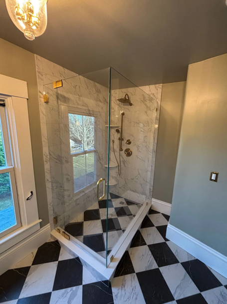Marble shower with glass doors, gold fixtures, checkered floor, window, and green walls.
