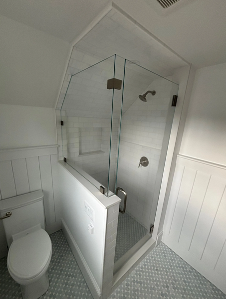 Modern bathroom with a glass shower, white walls, and blue tiled floor. Toilet is visible.