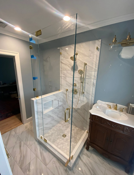 Newly renovated bathroom with a marble shower, gold fixtures, and a dark wood vanity.