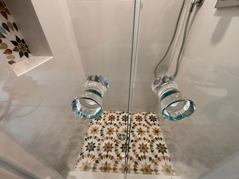 Shower interior with glass shower heads, ornate tile, and marble detailing.