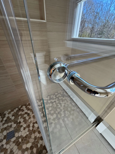 Shower door with chrome handle, glass panels, and stone tile floor.