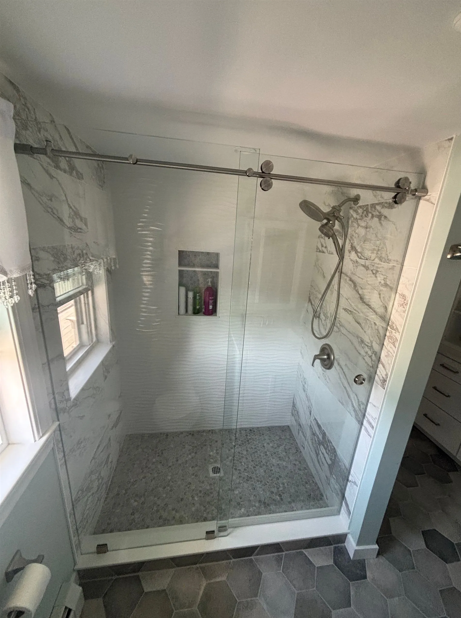 Modern walk-in shower with glass doors, marble-look tile, and pebble floor. Brushed nickel hardware.