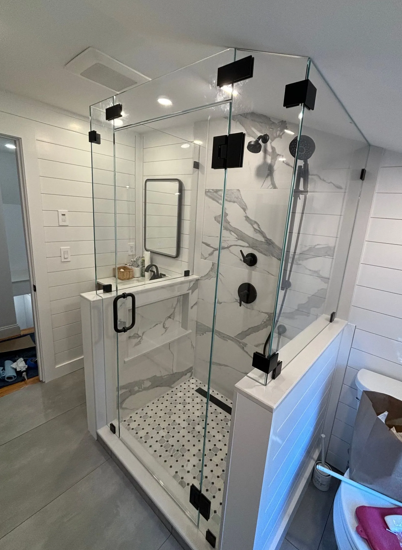Modern bathroom with glass shower enclosure, marble tile, black fixtures, and white walls.