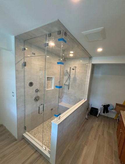 Newly remodeled glass shower with stone tile walls and pebble floor, and wood-look tile.