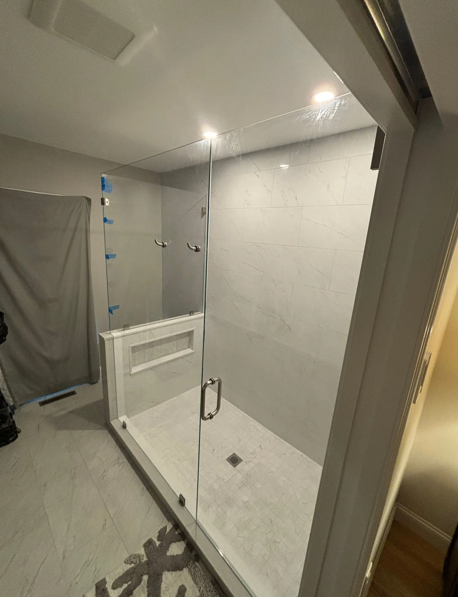 Modern, light-gray tiled shower with glass doors, a shelf, and a handle.