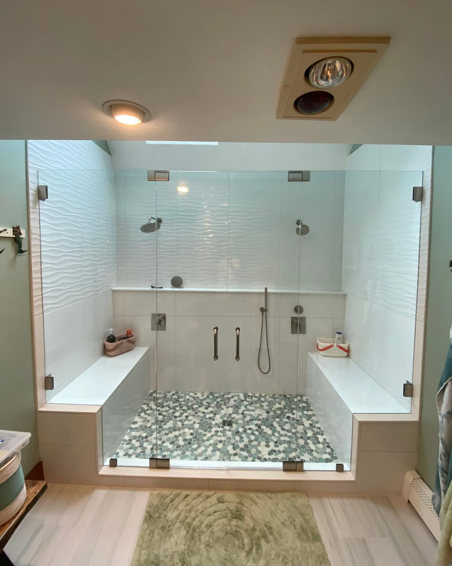 Spacious, accessible shower with glass doors, built-in benches, pebble floor, and multiple showerheads.