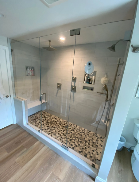 Spacious modern shower with glass doors, pebble floor, bench, and multiple shower heads.