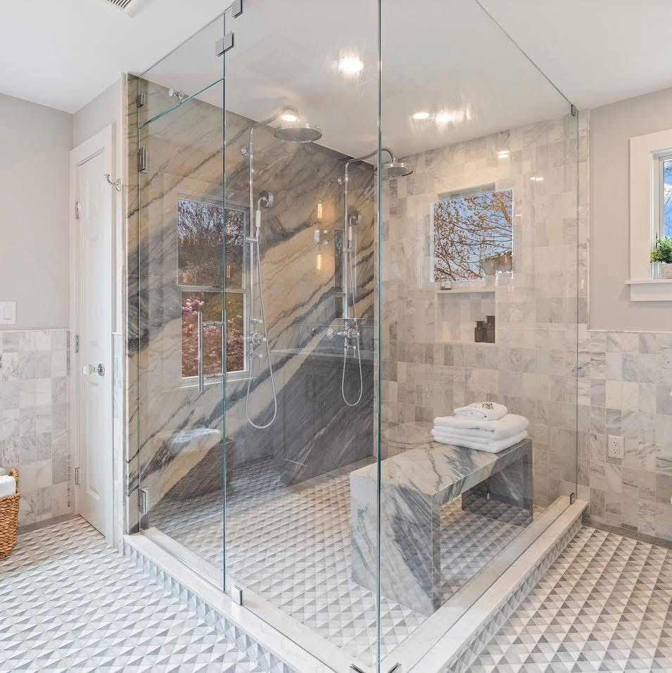 Luxurious bathroom with glass shower, marble walls and bench, and patterned tile floor.