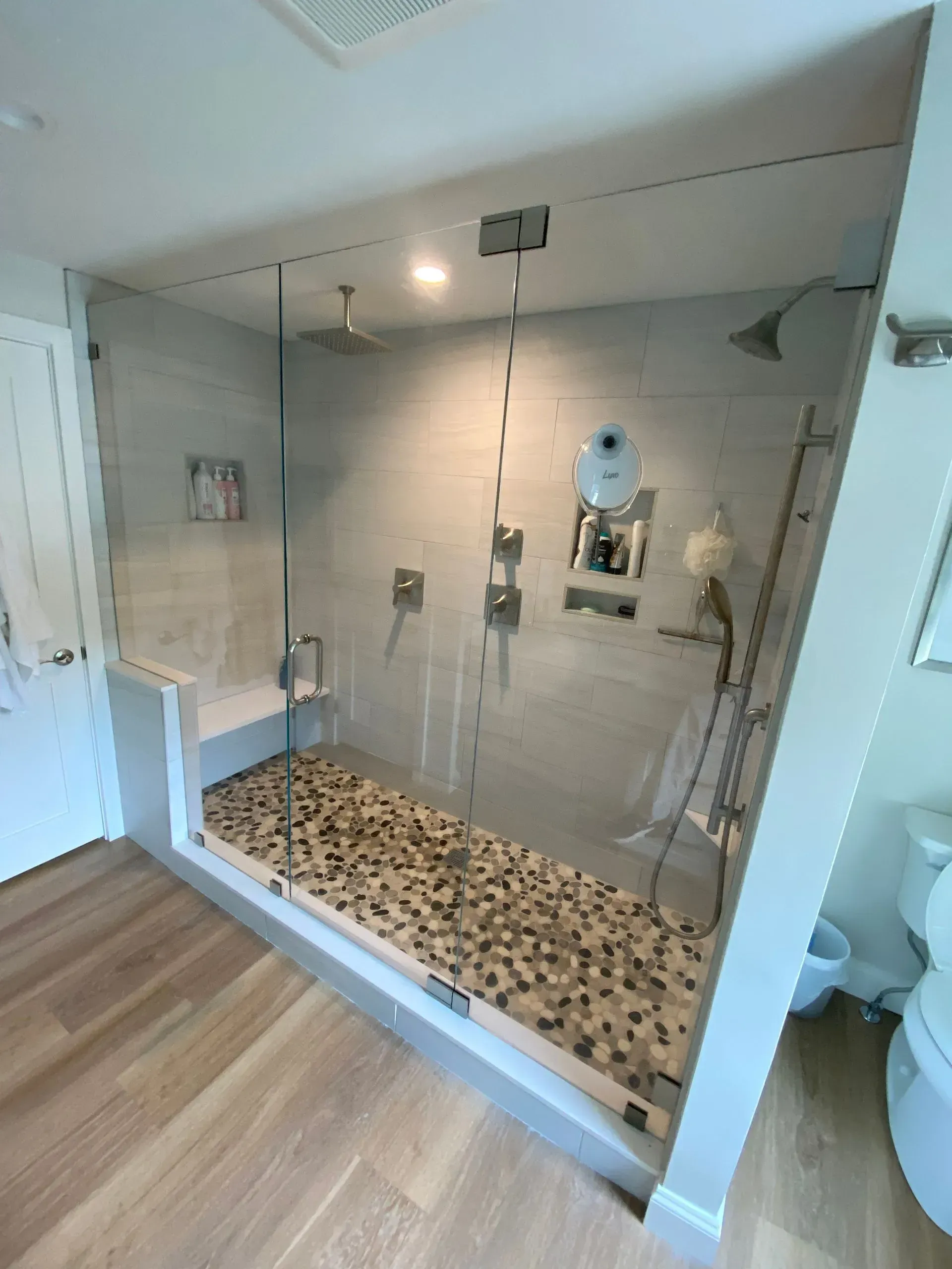Modern shower with glass doors and pebble floor; light gray walls, wooden floor.
