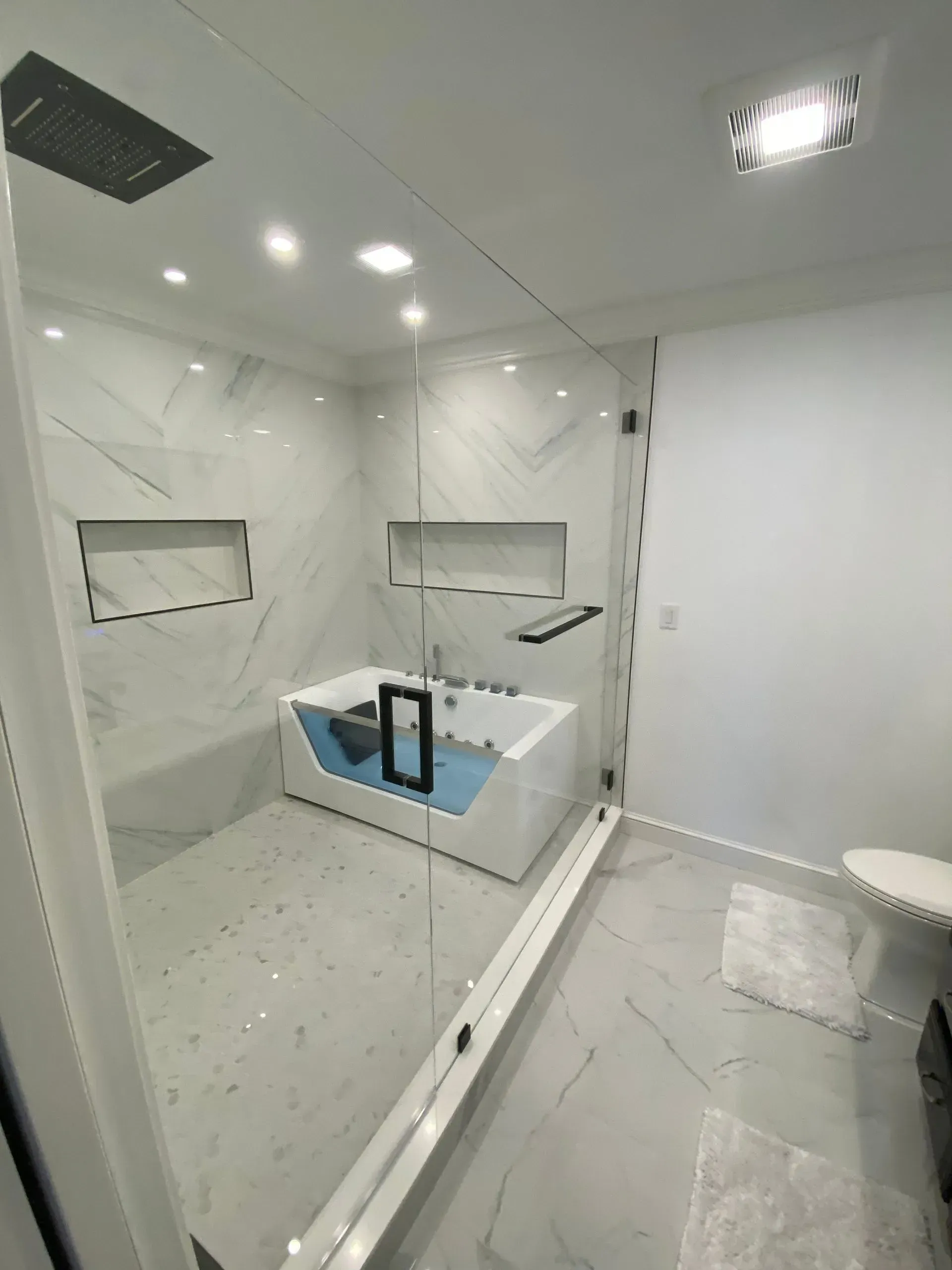 Modern bathroom with a glass-enclosed bathtub, marble walls, and recessed shelves.