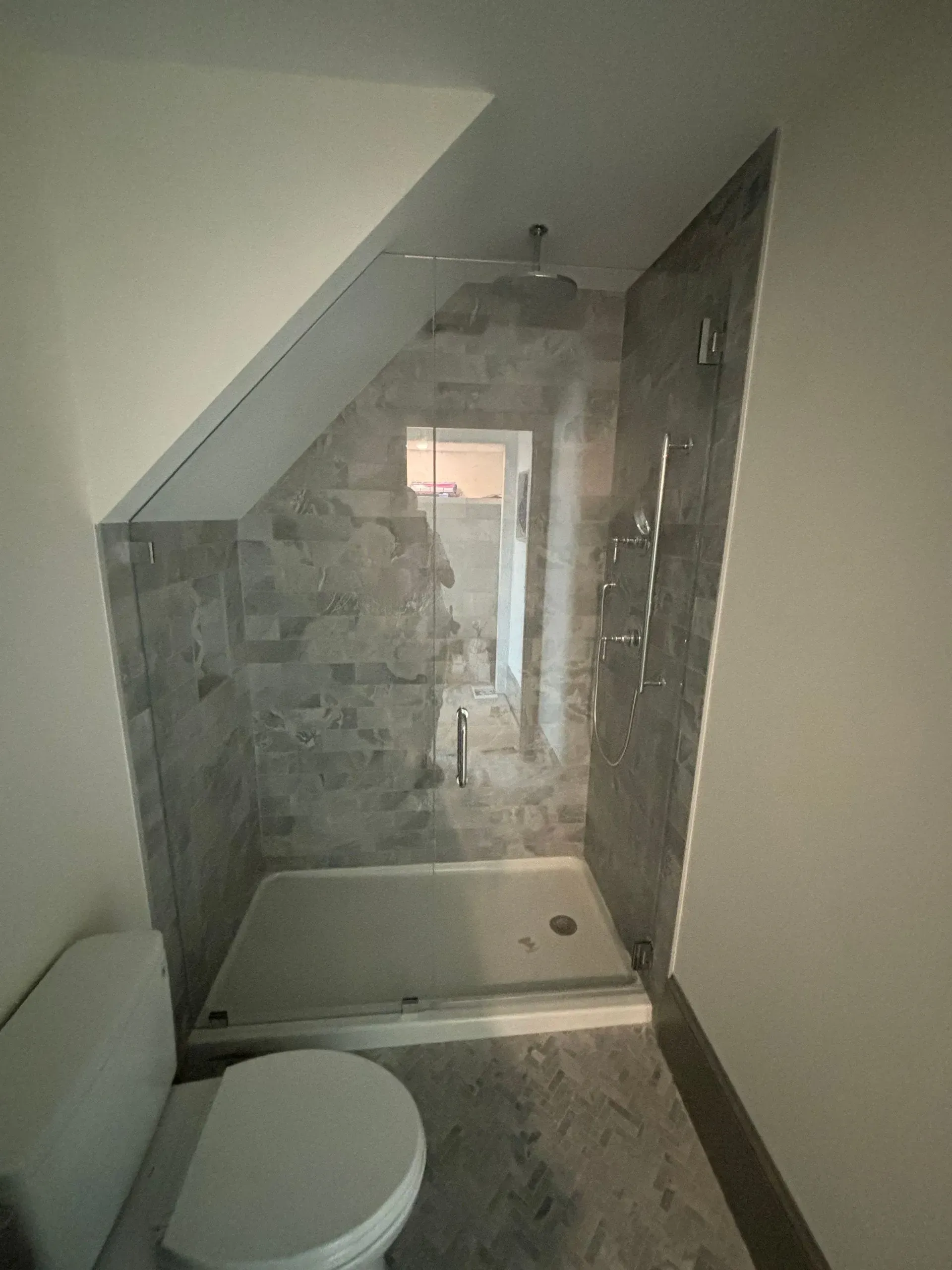 Small bathroom with angled ceiling, glass shower enclosure, gray tile, toilet.