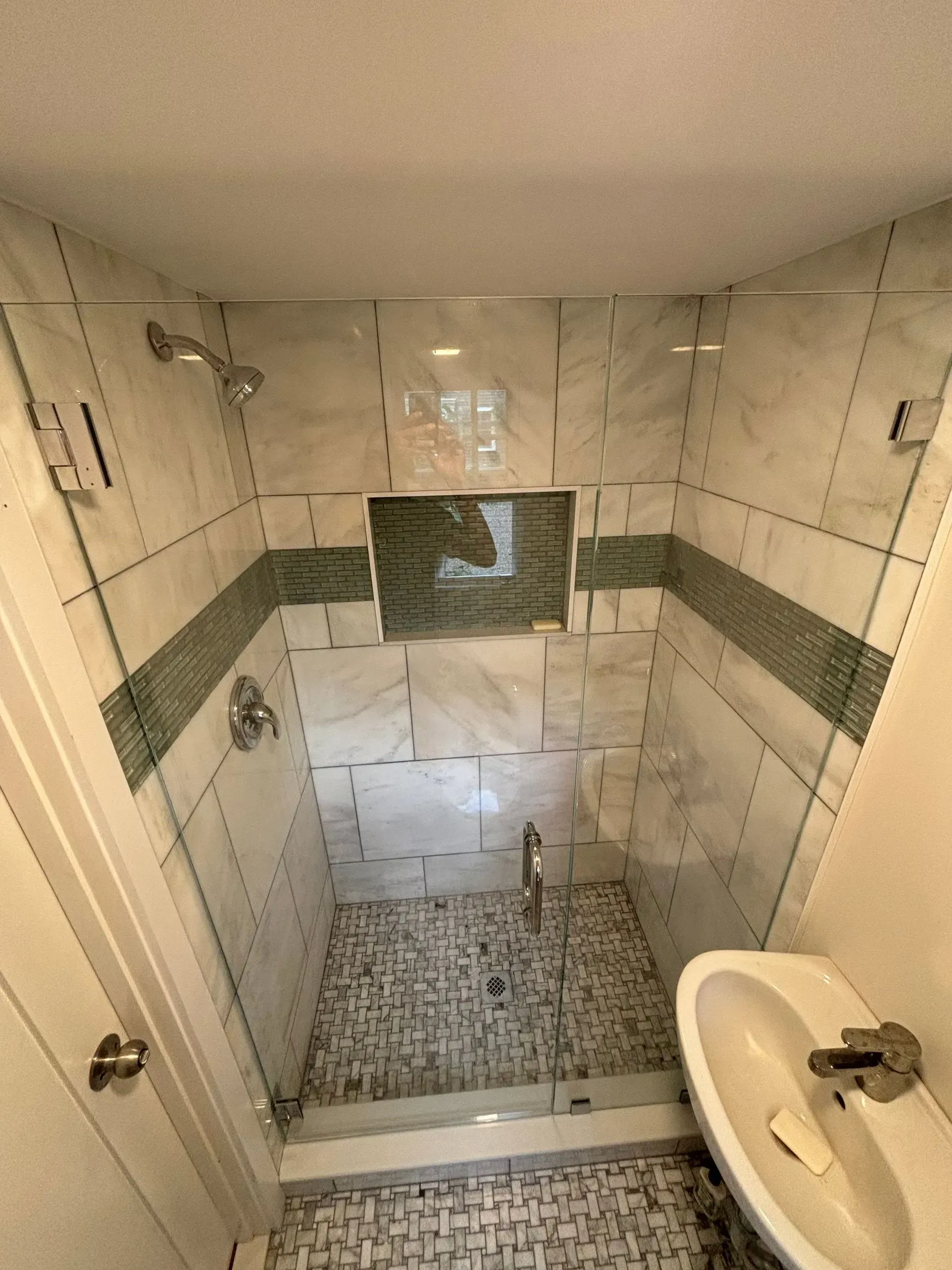 Shower with marble tile walls, glass doors, and a mosaic tile floor.