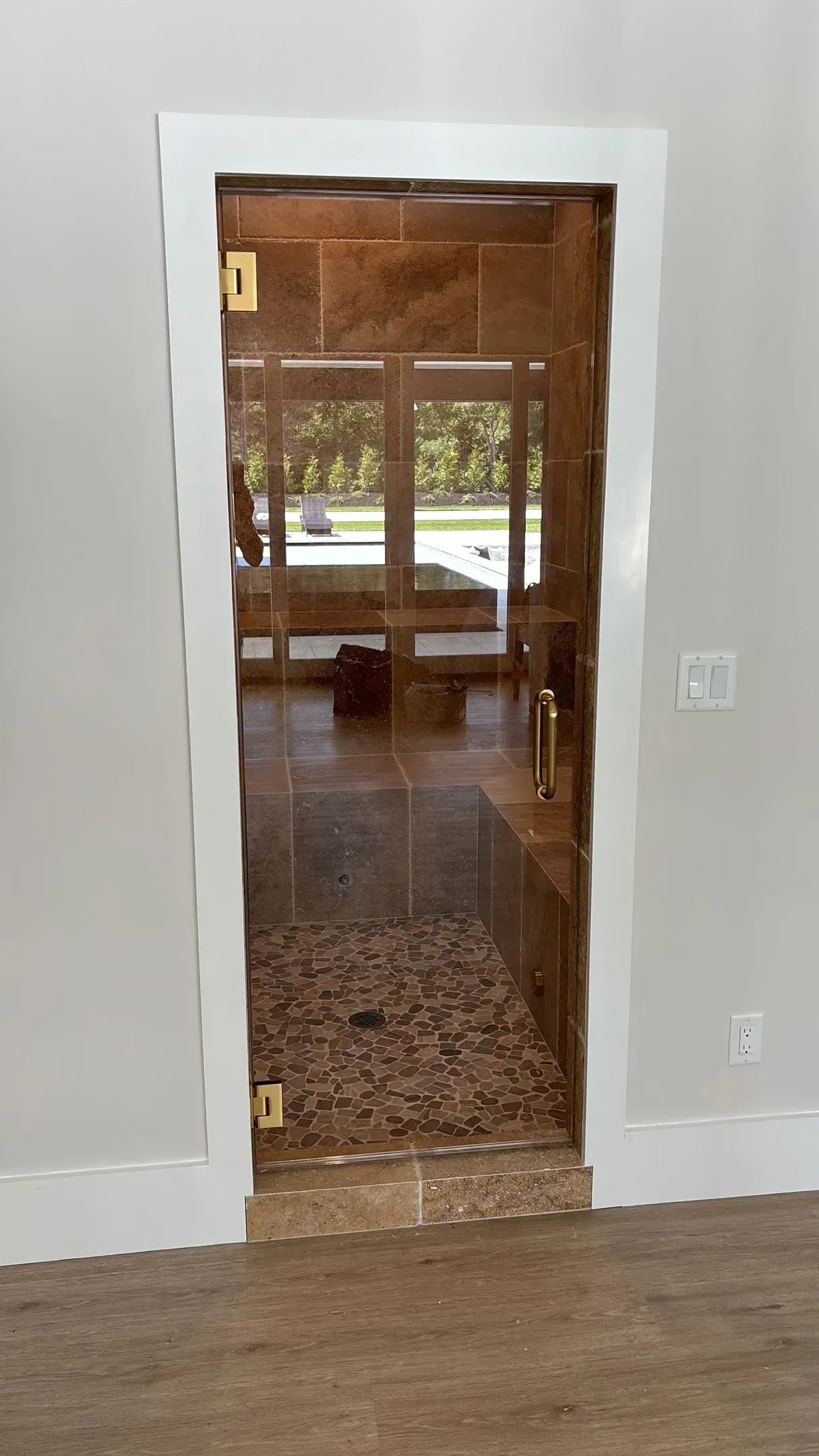 Framed glass shower door with gold hinges, beige and brown tile. The door is open, revealing the interior.