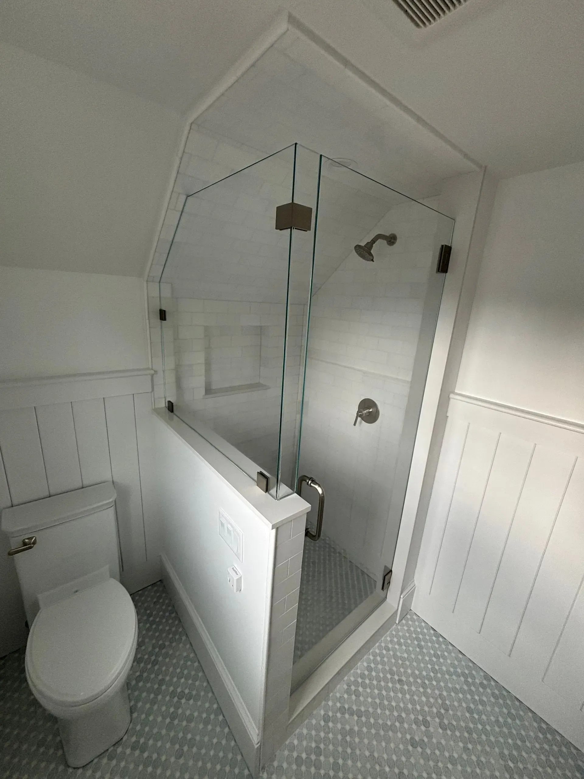 White bathroom with a clear glass shower, toilet, and blue tile flooring.