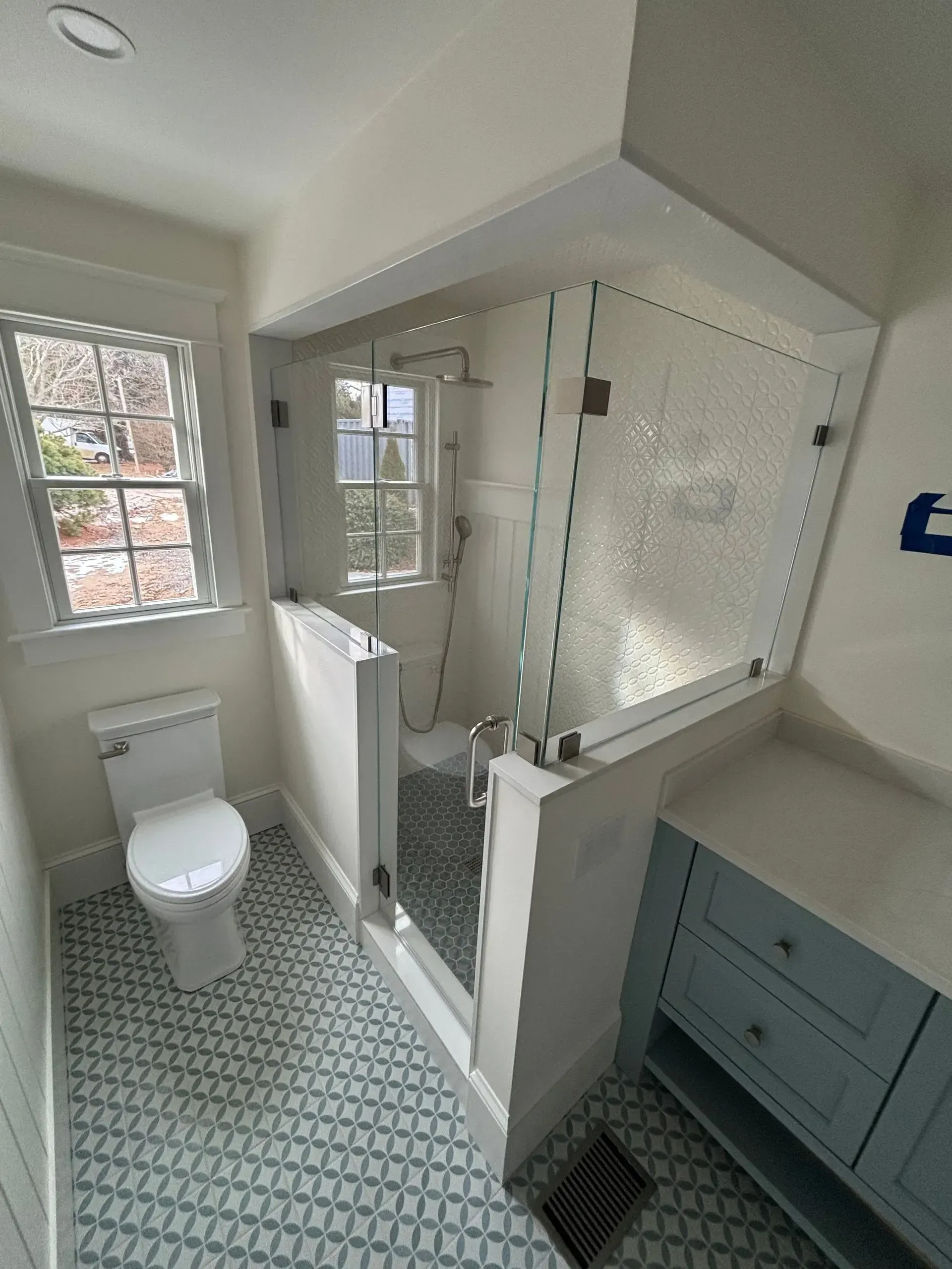 Bathroom with patterned blue and white floor tiles, a toilet, and a glass-enclosed shower.