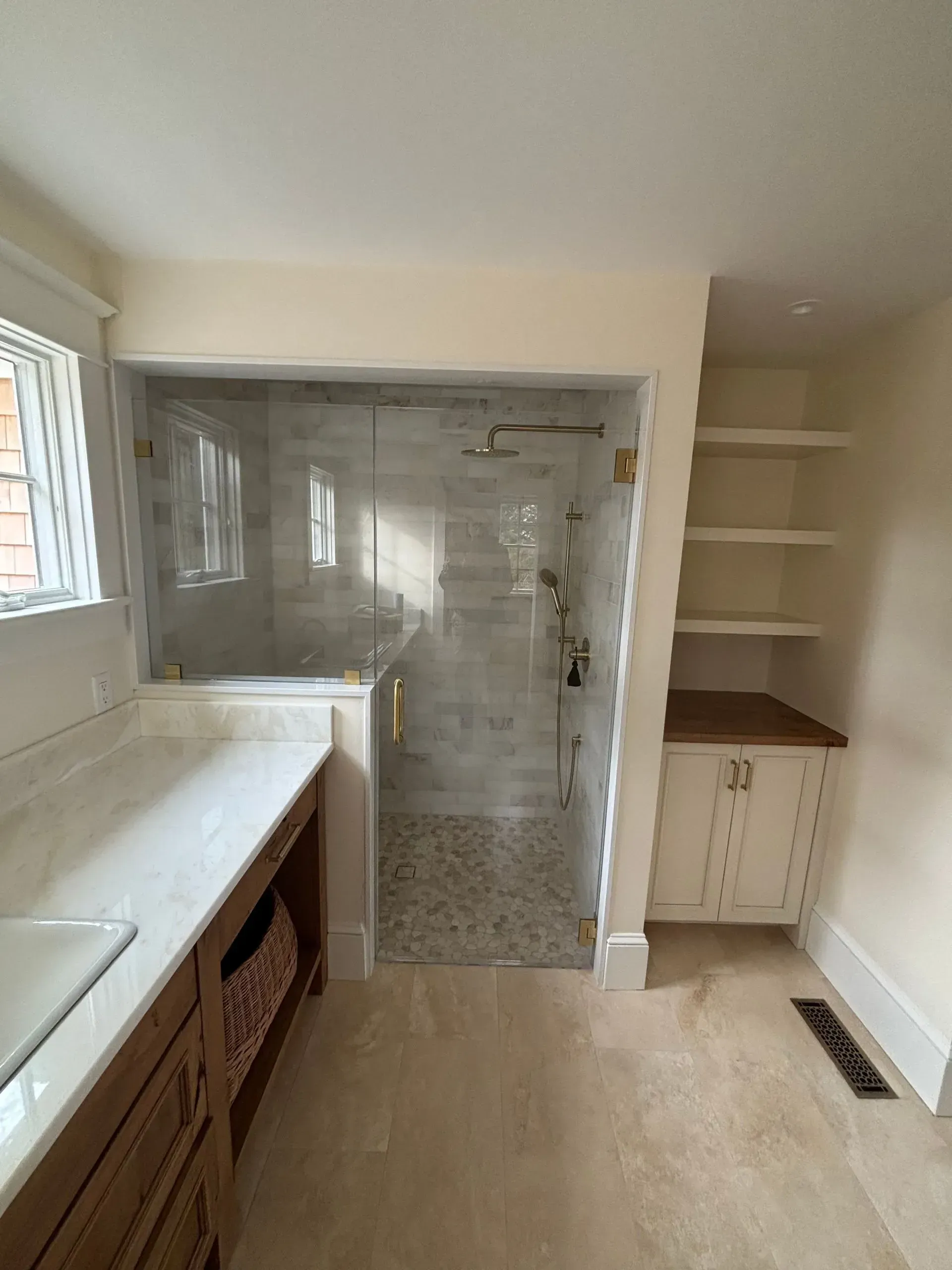 Bathroom with marble countertop, glass shower, and built-in shelves. Creamy walls and light floors.