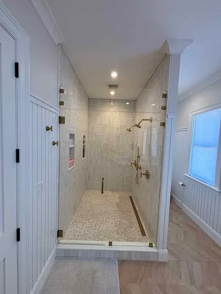 Modern bathroom with glass shower, light-colored tile, and gold fixtures.