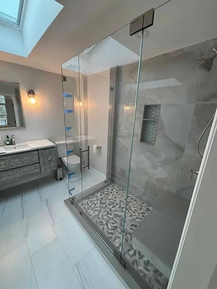 Modern bathroom with glass shower, gray marble, white tile, and skylight.