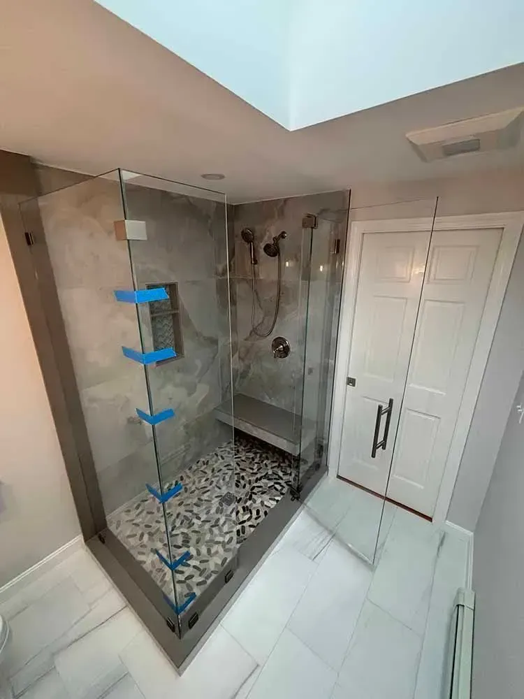 Modern bathroom with glass shower enclosure, pebble floor, gray tile, and white door.