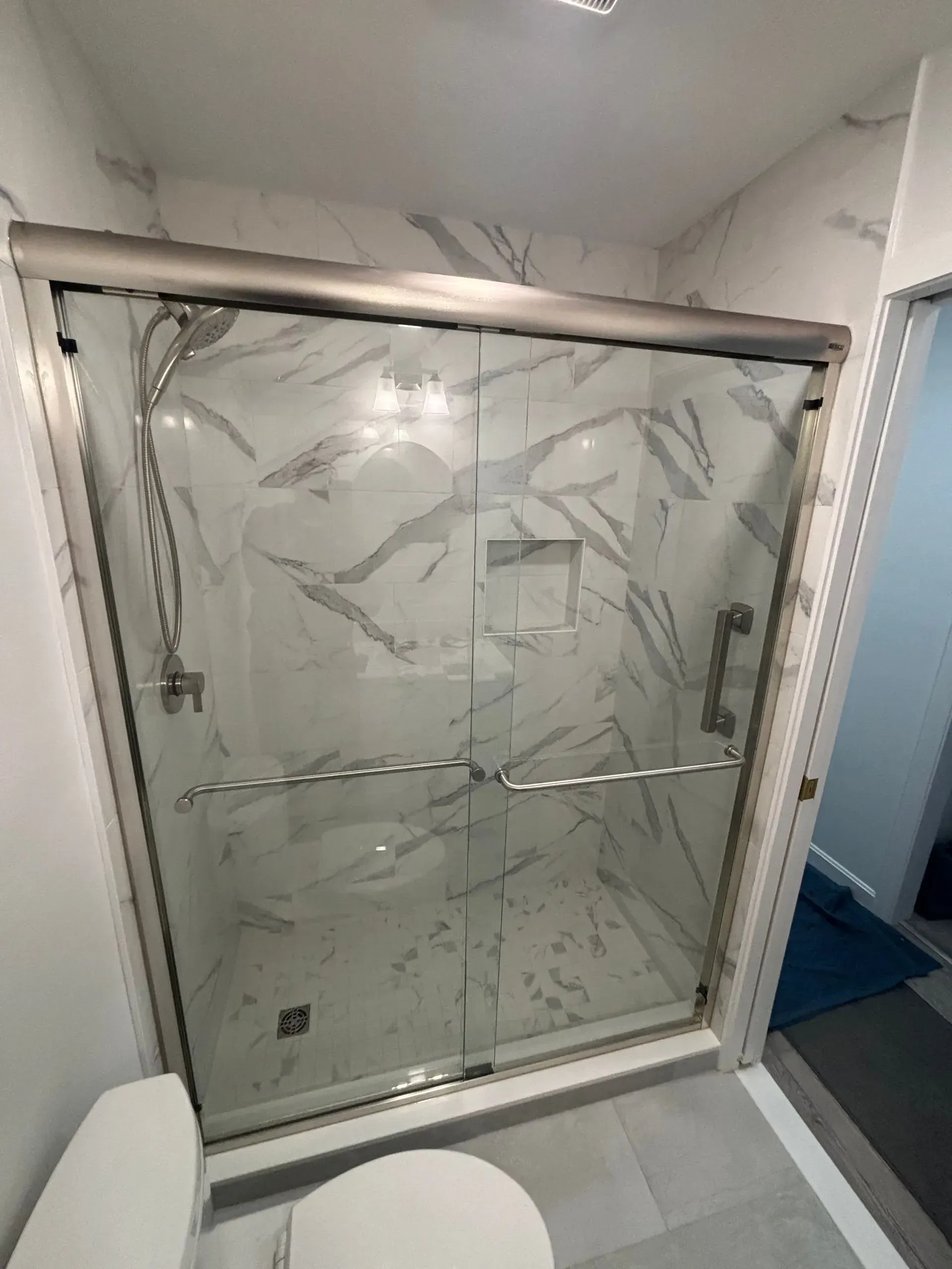 Bathroom with a glass shower enclosure, white marble tile, and a toilet.