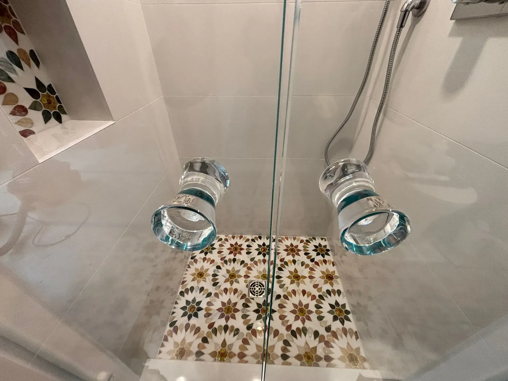 Glass-enclosed display with decorative mosaic tile and two clear spotlights above.