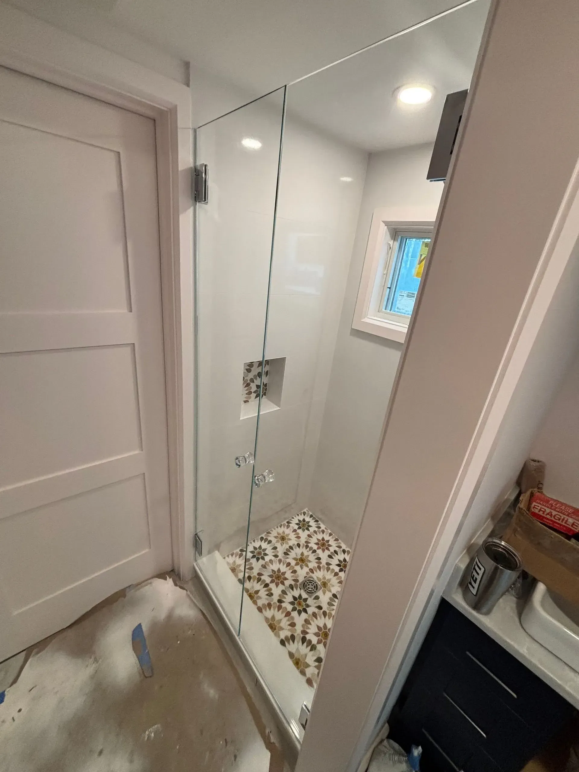 Glass shower enclosure in a small bathroom with decorative floor tile.