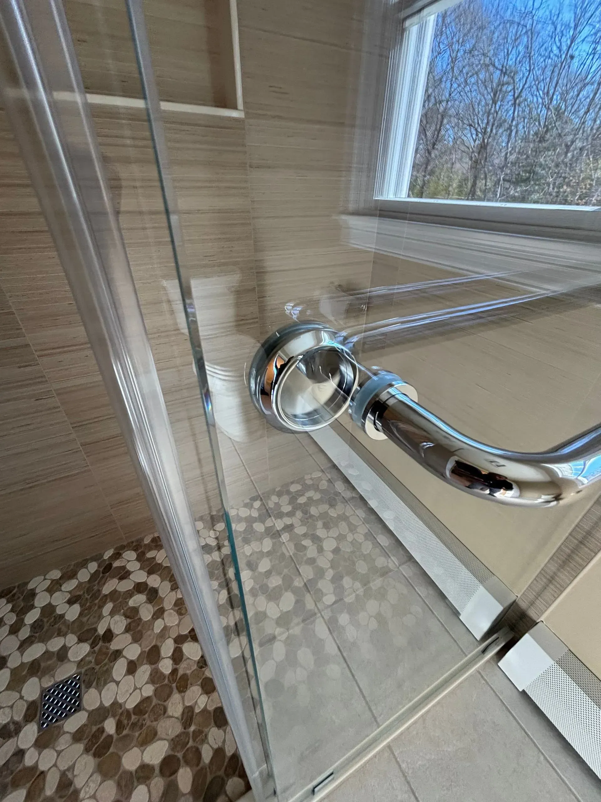 Glass shower door with chrome handle, pebble tile floor.