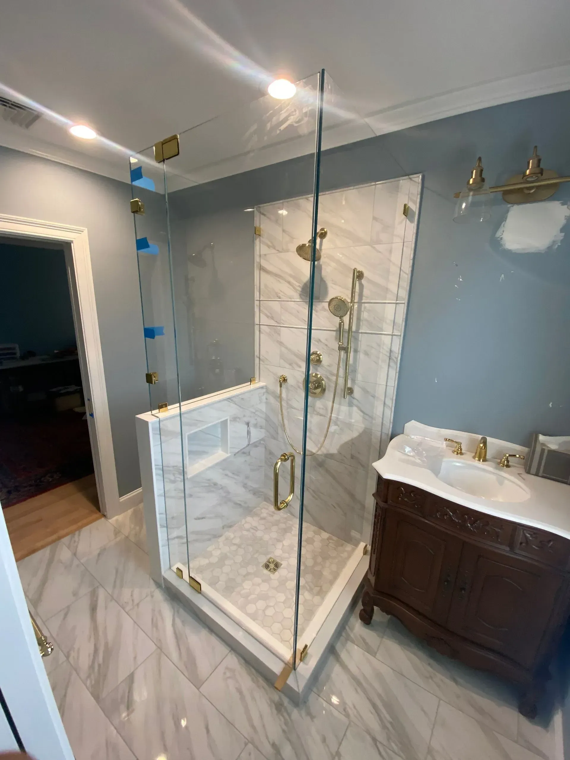 Newly renovated bathroom with marble shower, gold fixtures, and wood vanity.