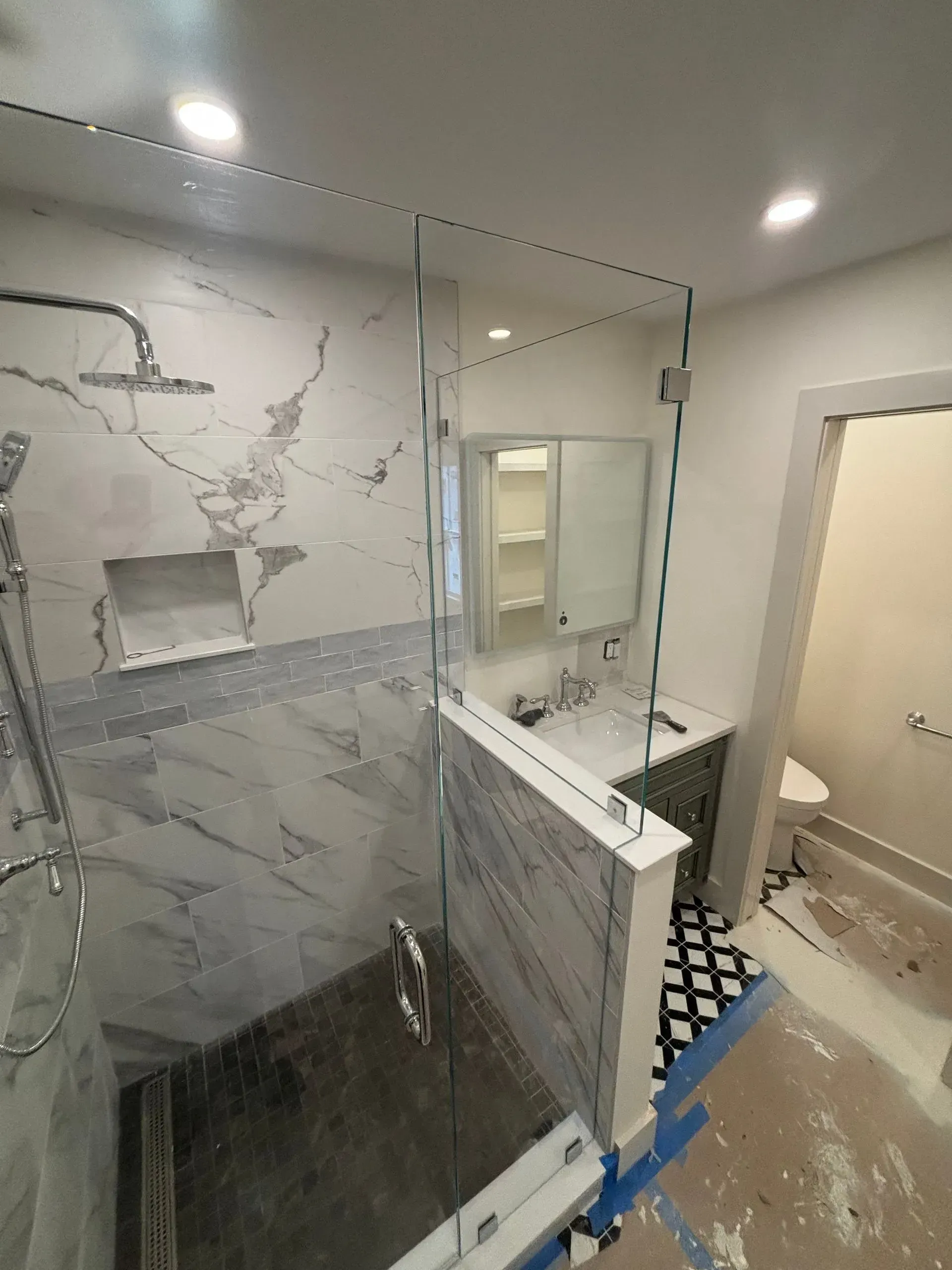 Modern bathroom with glass shower, marble tile, white walls, vanity, and toilet.