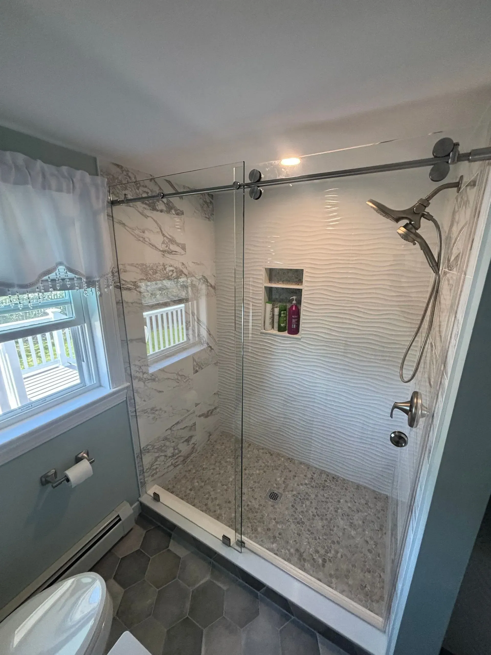 Modern shower with glass door, pebble floor, white tile walls, and chrome fixtures.