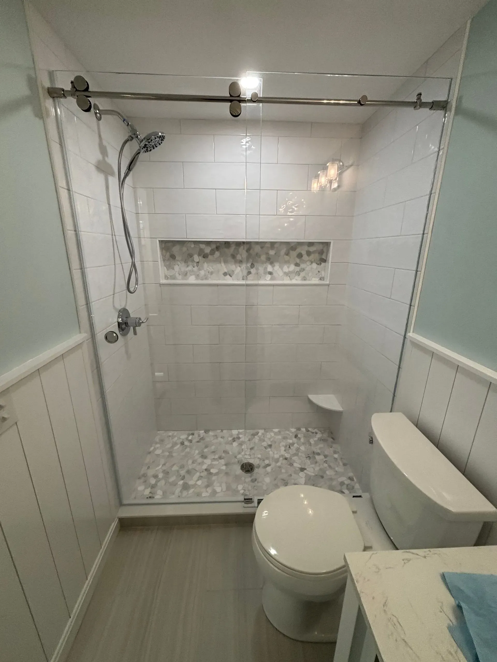 A small, white bathroom with a glass shower, pebble floor, and toilet.