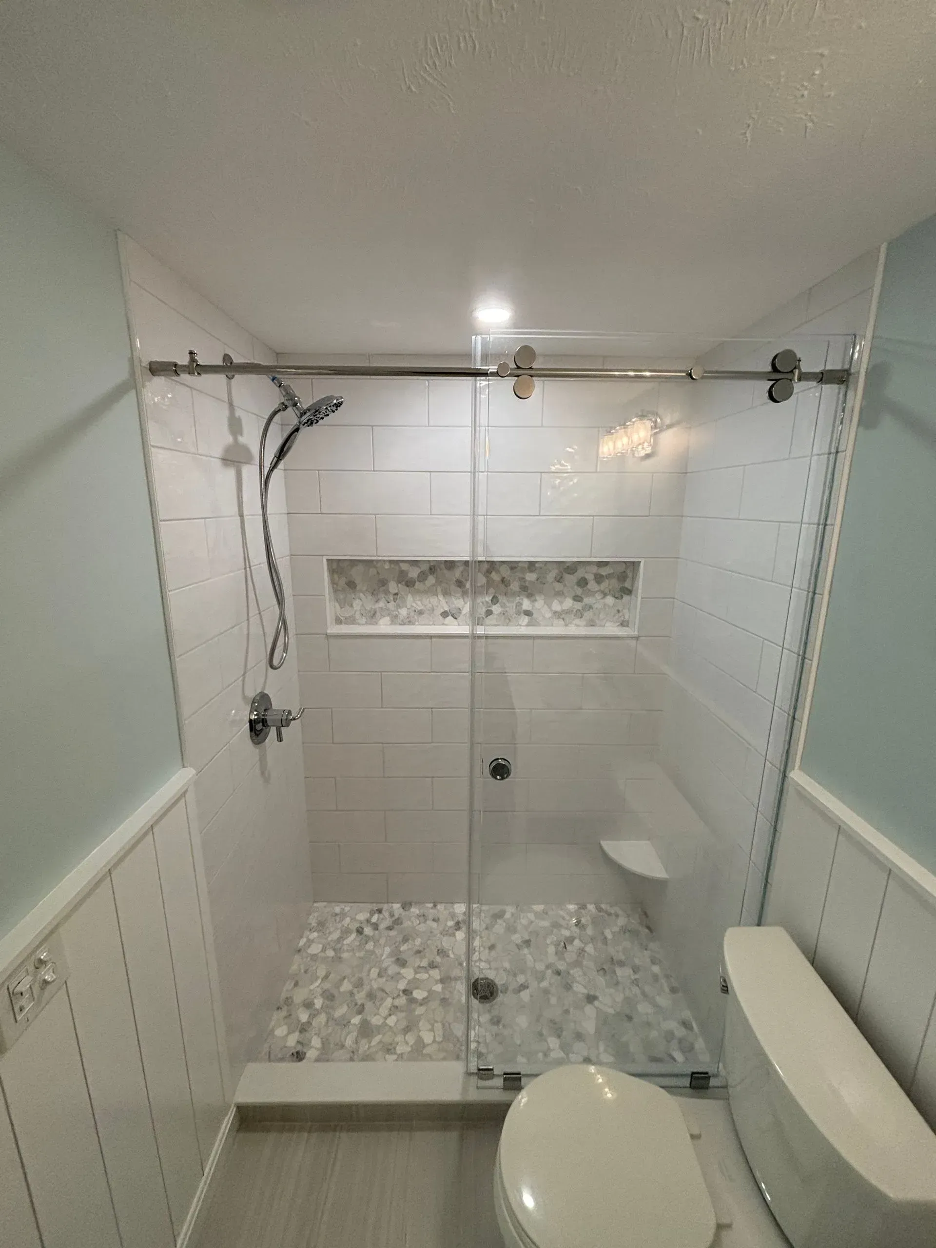Modern bathroom with glass shower, white subway tile, and stone floor.