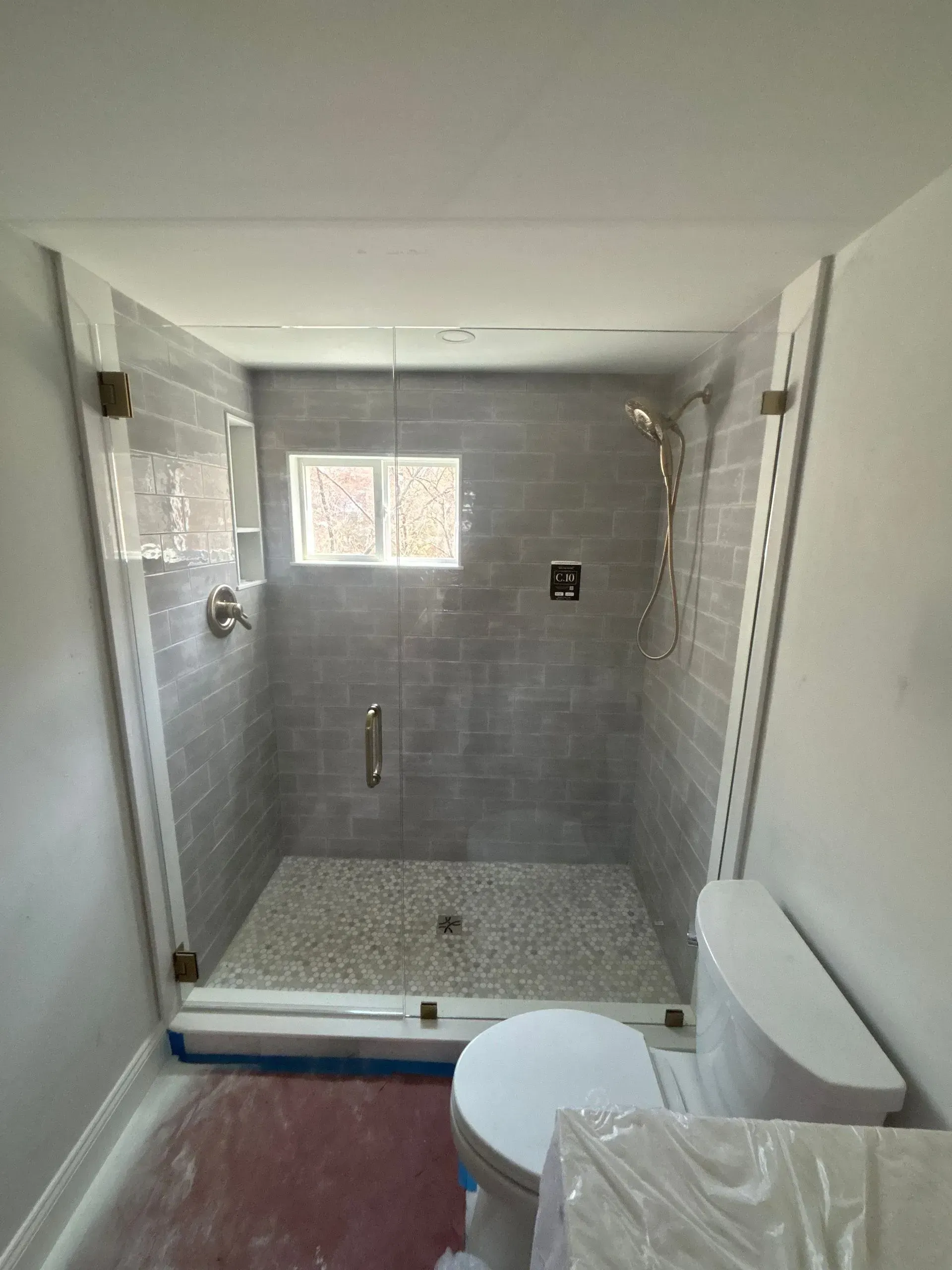 Newly renovated bathroom with a glass shower, gray tiled walls, and a white toilet.