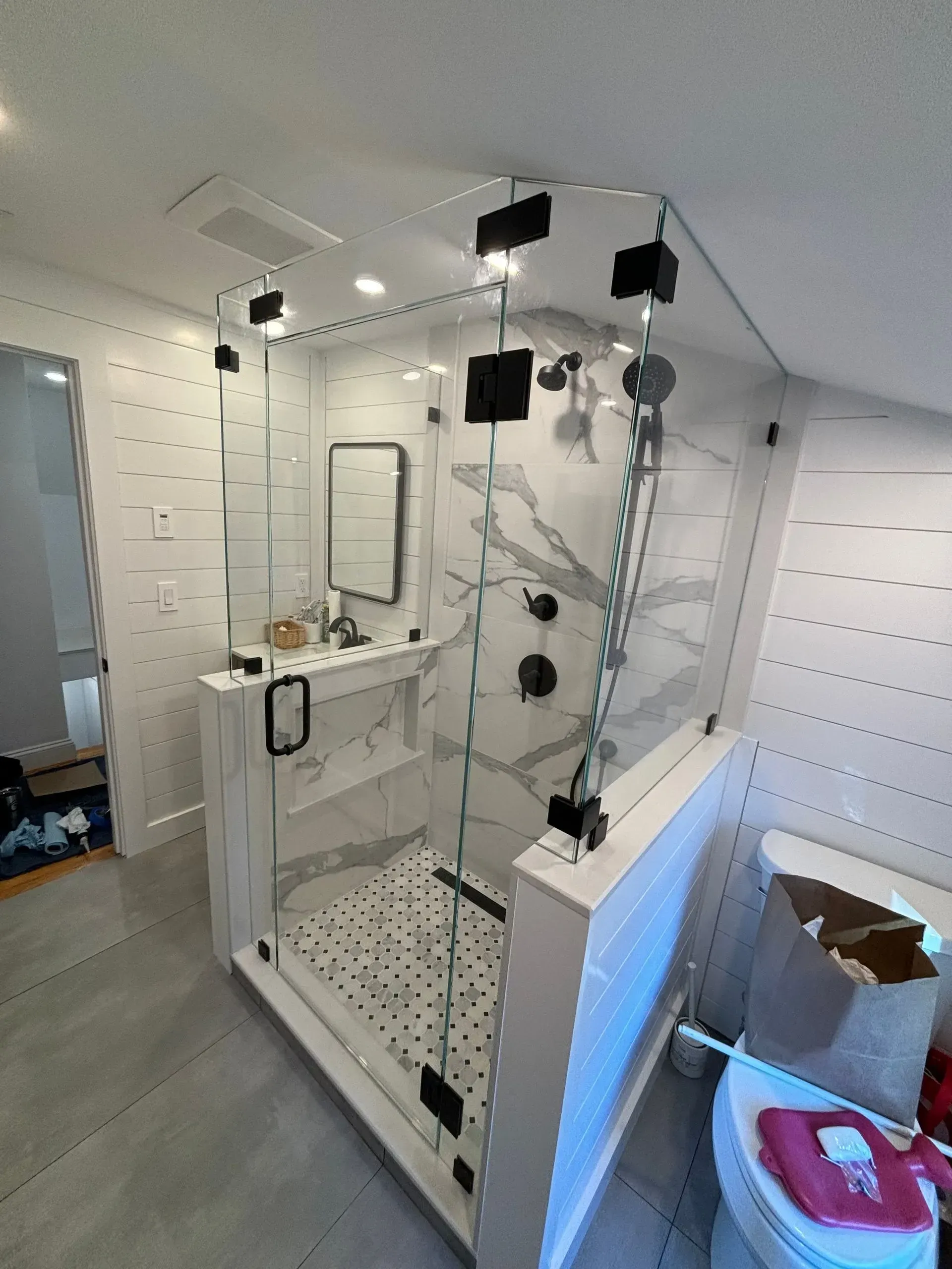 Modern bathroom with a glass shower, white and gray tiles, and black fixtures.