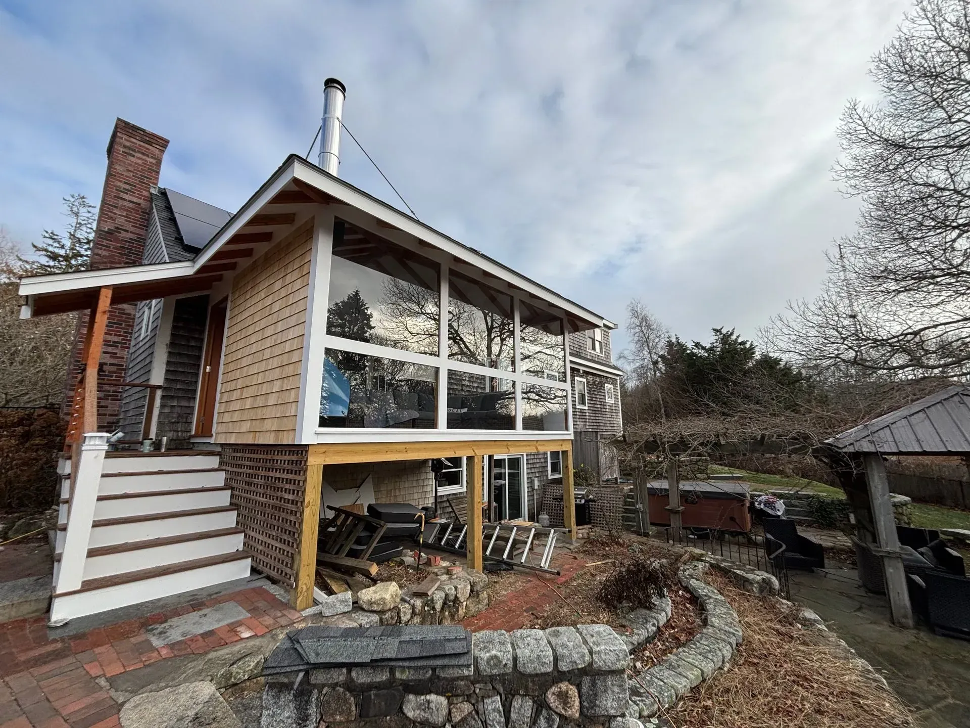 A house with a modern sunroom, brick chimney, and wooden deck. Cloudy sky above.
