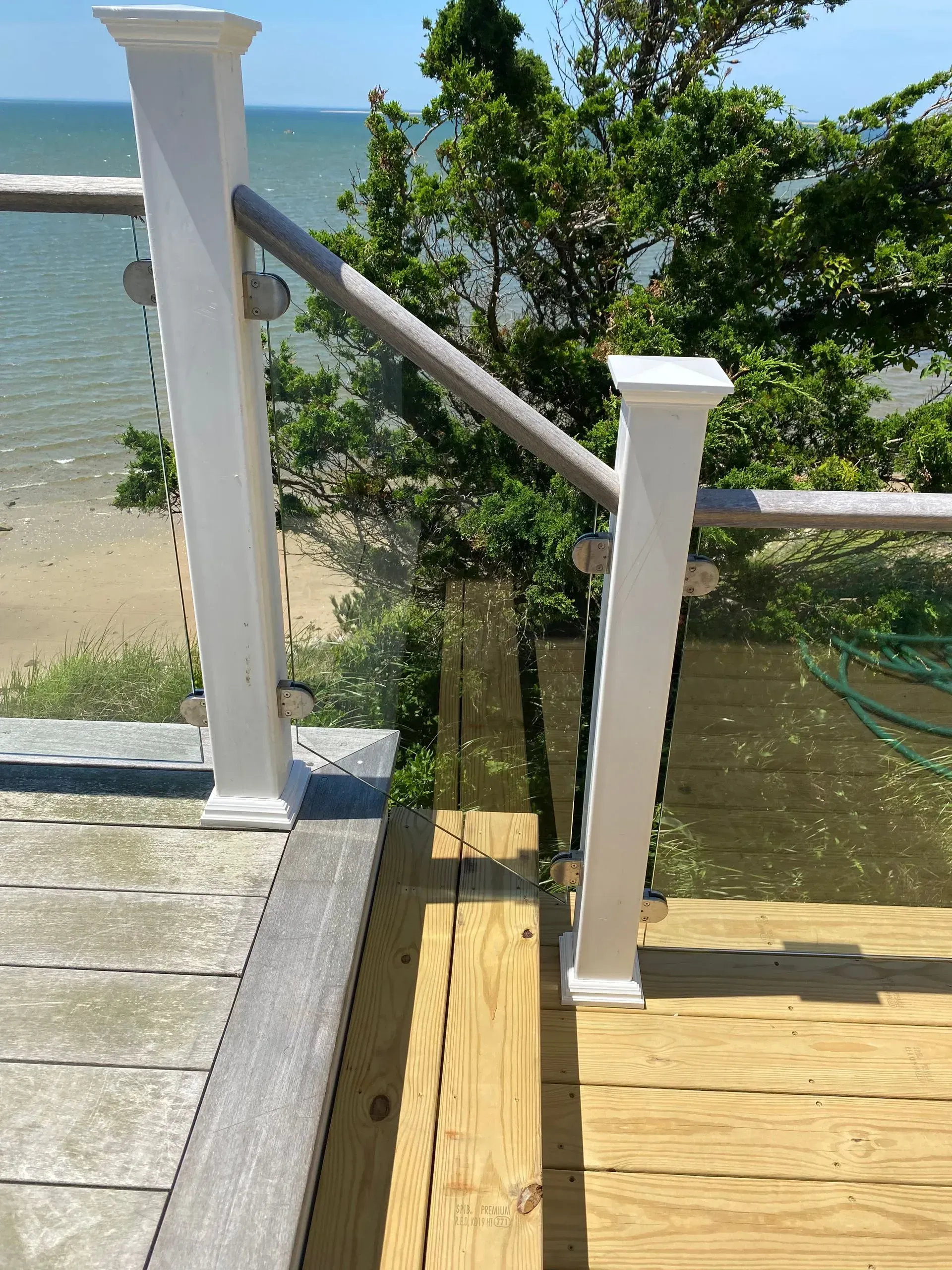 Wooden deck with white posts, glass panels, and a handrail overlooking the ocean.